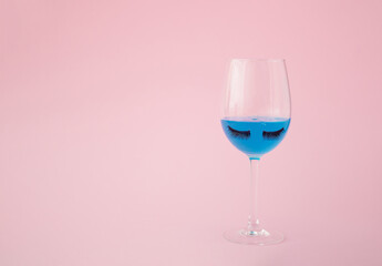 Champagne glass with eyelashes on pink background. Minimal party concept.