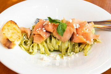 Fettucine with green healthy pesto sauce with smoke salmon on a white plate.