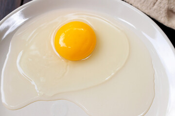 Organic free range egg and egg yolk on white dish; top view on wooden table background. 