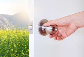 hand hold door knob to open white door to see the view of natural flower field and sun rise outside , explore new opportunity concept - obrazy, fototapety, plakaty