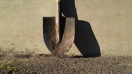 garden tool. old dirty shovel with clods of soil and shadow on cement wall background