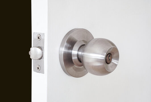 Stainless door knob with key hole on white wooden door ,opened with dark room background
