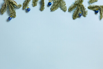 Frame from green Christmas fir tree branches wirh small blue New Year balls on blue colored background