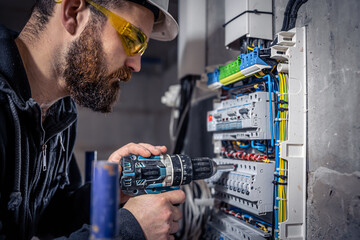 A male electrician works in a switchboard with an electrical connecting cable.