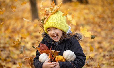 Little funny girl with pumpkins in the autumn forest on a blurred background.