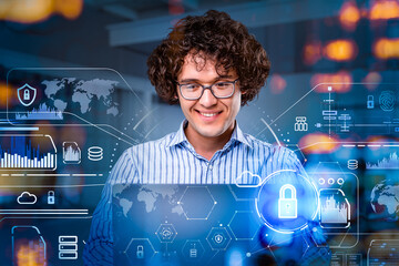 Portrait of smiling businessman in glasses is sitting in front of laptop at abstract office space, white and blue glowing information protection icons. Concept of cyber security and data storage