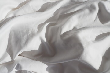 Closeup of beautiful white shiny crumpled polyester fabric sheets on the bed with warm motion and...