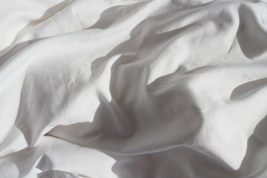 Closeup Of Beautiful White Shiny Crumpled Polyester Fabric Sheets On The Bed With Warm Motion And Feeling For Background And Decoration Cloth Washing And Laundry Concept At Home