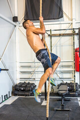 Rope climbing, male bodybuilder climbing a rope in a gym