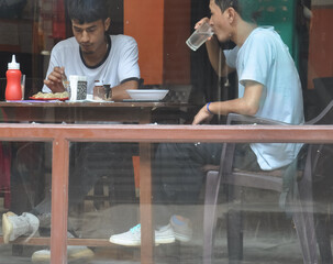 View of people eating food in the cafe seen through the window glass.