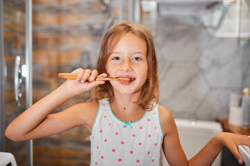 Little Girl brushing teeth with ecologe wooden Toothbrush in the bathroom at home, healthy hygiene...