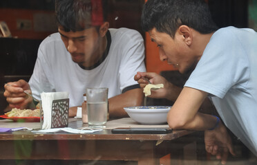 Fototapeta na wymiar Two young guys eating fast food at indoor cafe seen through window glass