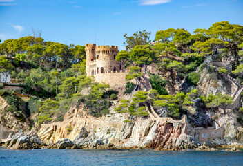 Fototapeta na wymiar Beautiful wild rocks with castle Sant Joan and coniferous trees on Mediterranean coast in Lloret de Mar, Costa Brava, Spain