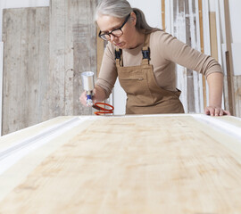 wood crafts, woman artisan carpenter painting with spray gun paint white the door in her workshop,...