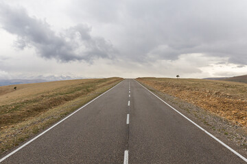Classic panoramic view of a straight desert road rushing to the horizon in the middle of a stone land on a cloudy day