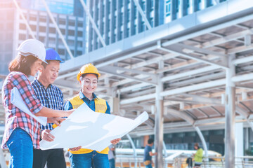 Engineer and worker team with helmet looking paper plans at construction site.