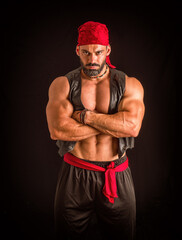 Fototapeta na wymiar Muscular male pirate in studio shot, wearing bandana and open vest