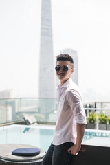 Handsome young Asian man standing in the rooftop bar near the swimming pool. Chinese guy, millennials life, lifestyle in the big city, Modern Asia