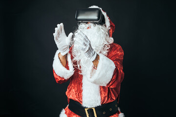 Man dressed as Santa Claus with virtual reality glasses, on black background. Concept of Christmas, Santa Claus, gifts, celebration.