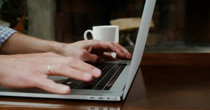 A man dressed in casual clothes, is typing on a laptop at hom