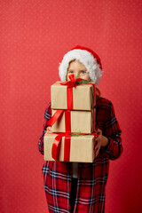 Funny little girl in santa hat with many Christmas gift boxes isolated on red background,