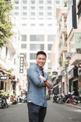 Portrait of asian young handsome man in denim shirt standing on the street with crossed hands, smiling and looking at camera with copy space.