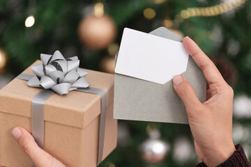 Hand holding mockup christmas greeting card and gift box for invitation design on christmas tree...