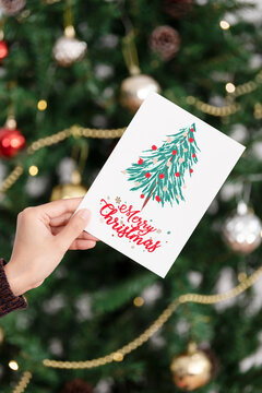 Hand holding christmas greeting card on christmas tree background.