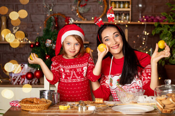 mom and daughter eat tangerines in a dark kitchen with a Christmas tree for New Year or Christmas, smile, fool around and have fun together in anticipation of the holiday in a Santa Claus hat