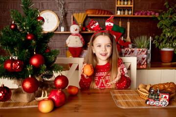 Fototapeta na wymiar a girl child plays or eats tangerines in a dark kitchen under a Christmas tree with red balls, the concept of new year and Christmas