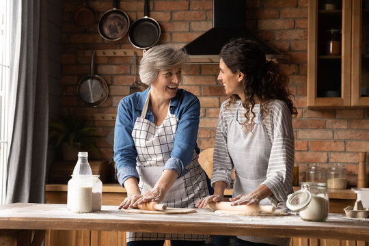Cheerful Hispanic older 60s mom and grown daughter cooking homemade bakery food, dessert for family dinner, talking, chatting, laughing, enjoying time together, household, baking activities