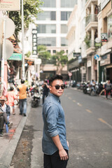 Fototapeta premium Portrait of asian young handsome man in denim shirt and sunglasses standing on the street and looking at camera with copy space. Chinese people