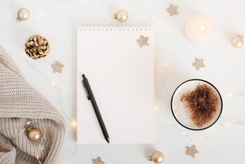 White sheet of notebook with pen on white table with cup of cocoa or coffee, candle and festive...