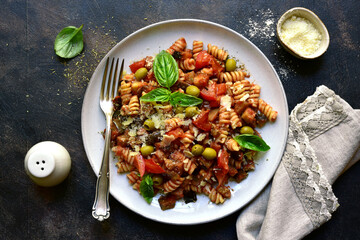 Fusilli pasta with tomatoes, eggplants and olives. Top view with copy space.