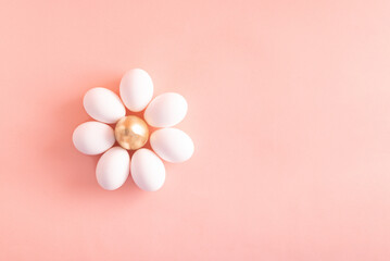 White eggs and a golden one forming an abstract daisy flower against pastel pink background. Minimal creative layout.