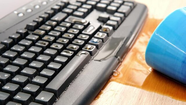 closeup female hands of elderly woman typing text on computer keyboard, cup of coffee, tea suddenly spills, hot liquid spoils equipment, concept of need to repair gadget, an accident at workplace