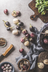 Fototapeta na wymiar Cooking with eggplant: purple and striped eggplant on kitchen table with dish cloth, knife, cutting board and garlic. Healthy cooking at home with seasonal summer vegetables. Top view.