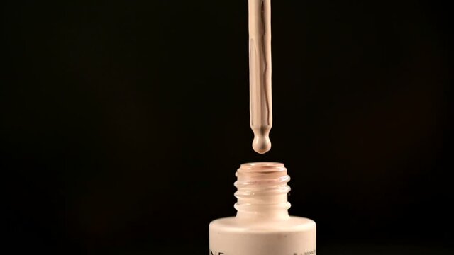 A drop of tonal cosmetic foundation close-up, close-up, falls into a jar. Dark background