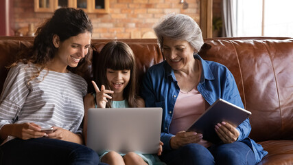 Happy kid girl, young mother, older grandmother using digital devices, laptop, tablet, making video...