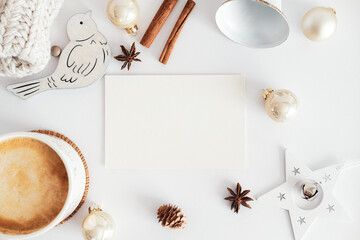 Obraz na płótnie Canvas Blank greeting card mockup, cinnamon sticks, Christmas decorations, cup of hot chocolate on white desk table. Hygge, cozy home, nordic style concept.