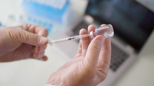 Top view of a doctor's hands in gloves. He draws the vaccine into a syringe.