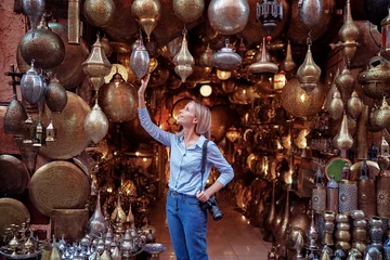 Fototapeten Travel and shopping. Young traveling woman with choose presents in copper souvenir handicraft shop in Morocco. © luengo_ua