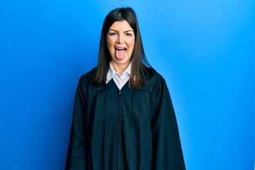 Young hispanic woman wearing judge uniform sticking tongue out happy with funny expression. emotion concept.