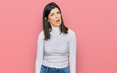 Beautiful brunette woman wearing casual clothes in shock face, looking skeptical and sarcastic,...