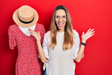 Beautiful hispanic woman standing by manikin celebrating victory with happy smile and winner expression with raised hands