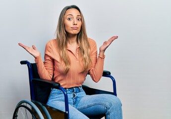 Beautiful hispanic woman sitting on wheelchair clueless and confused with open arms, no idea and...
