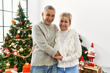 Obraz na płótnie Canvas Middle age caucasian couple smiling happy and hugging celebrating christmas at home.