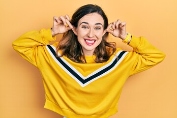 Young hispanic girl wearing casual clothes smiling pulling ears with fingers, funny gesture....