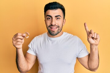 Young hispanic man holding deafness headset smiling with an idea or question pointing finger with happy face, number one