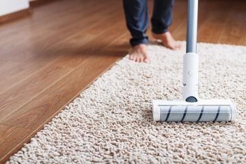 Human legs and a white turbo brush of a cordless vacuum cleaner cleans the carpet in the house